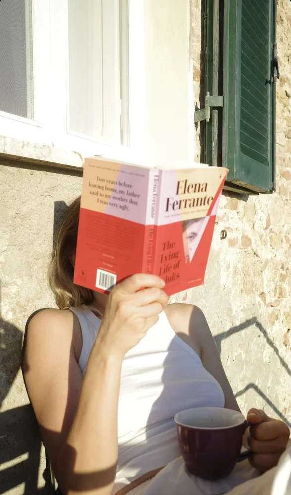 Tess reading Elena Ferrante in the sun with a cup of coffee